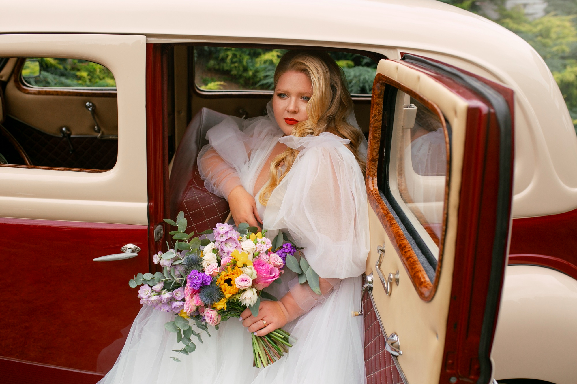 A woman in a wedding dress sitting in a red and white car before her 1980s Vegas wedding.